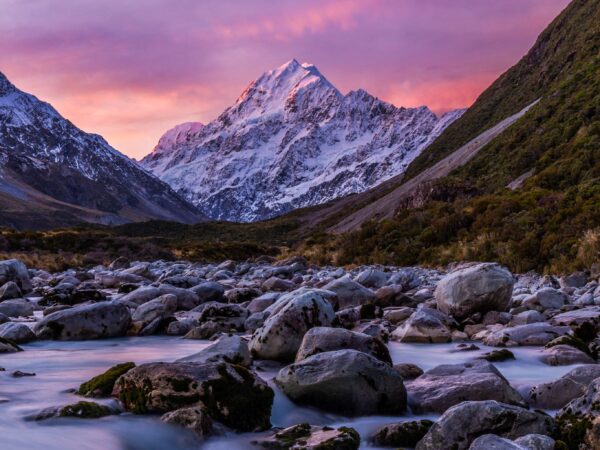 Snowy mountain and rocky stream at sunset