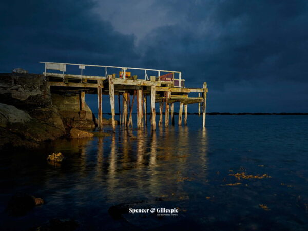 Old wharf over dark, calm water at sunset.