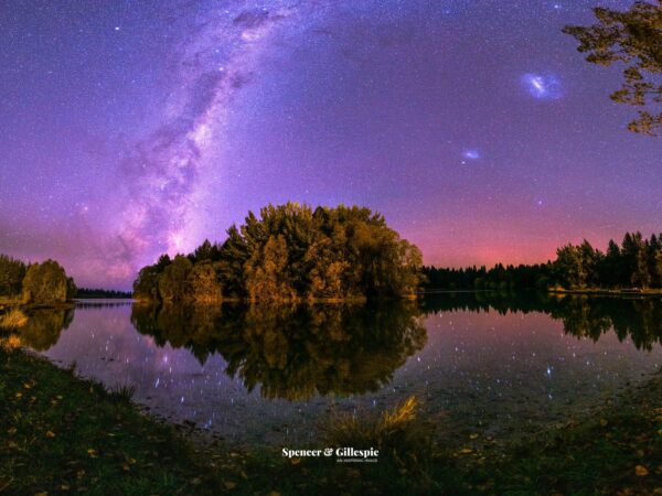 Starry night sky over calm lake with trees