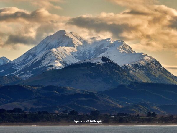 Snowy mountains with green hills and cloudy sky.