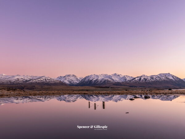 Snowy mountains reflected in calm lake at sunrise.