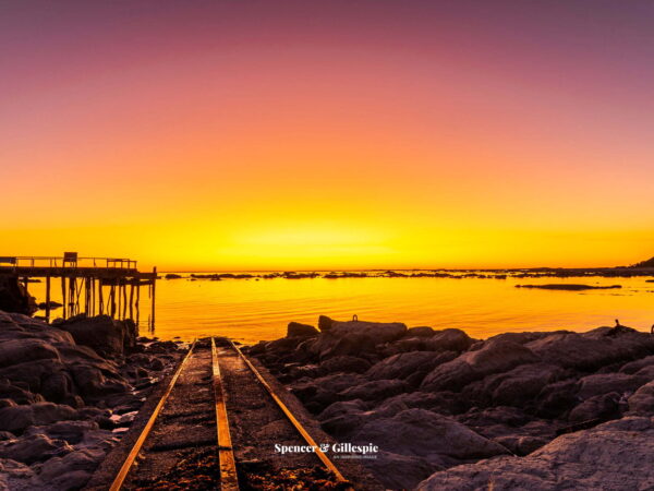 Sunset over rocky coastline and pier.