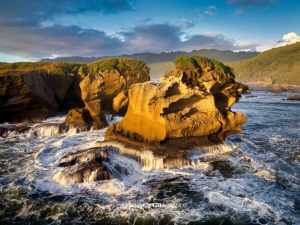 Rocky coastal cliffs with waves, covered in greenery.