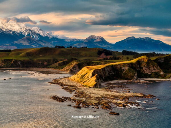 Scenic coastal cliffs with snowy mountains in New Zealand.