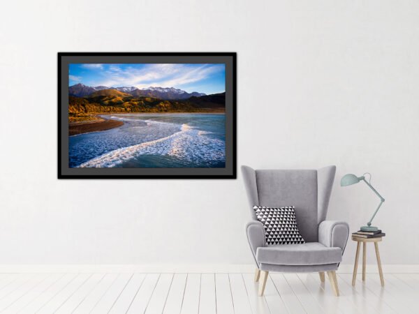 Framed seascape painting on wall above grey armchair.