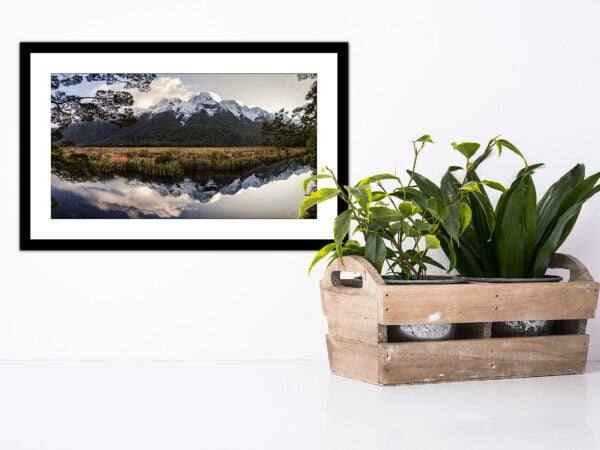 Framed landscape photo with houseplants on white background.