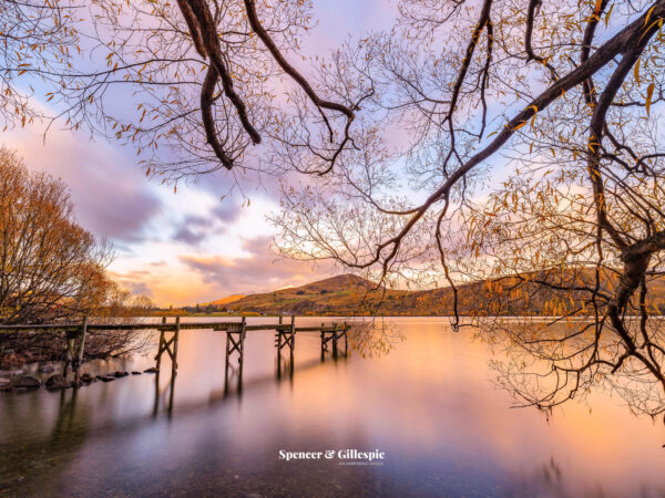 Sunset over serene lake with wooden pier.