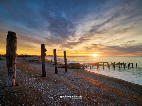 Sunset on a rocky beach with wooden pilings.